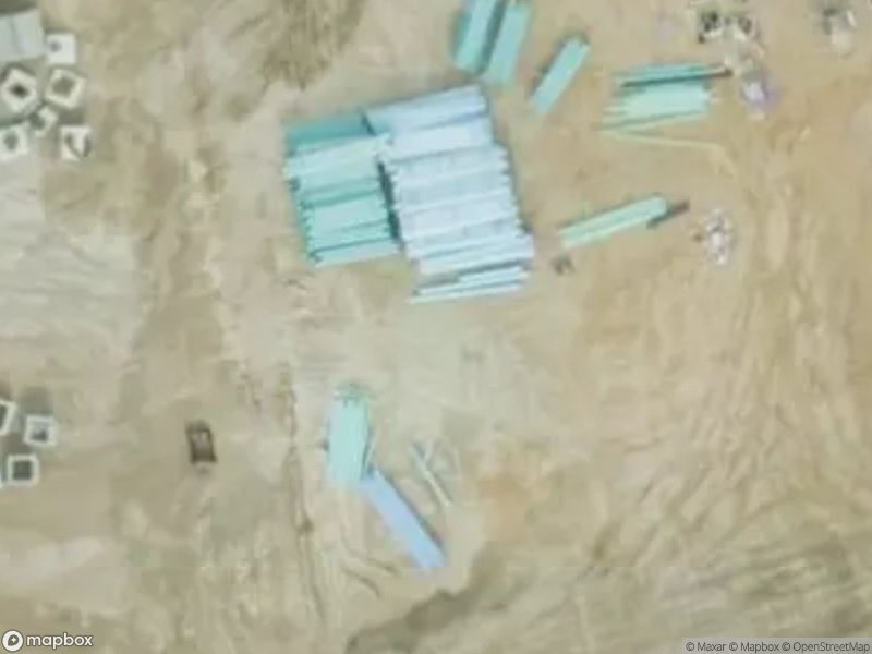 Aerial view of construction materials, including stacked pipes and scattered items on a sandy surface.