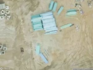 Aerial view of stacked materials and scattered objects on a sandy surface.