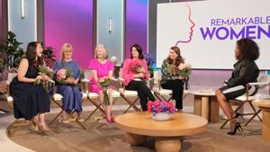 Six women sit in a studio, holding flowers and engaging in conversation. A "Remarkable Women" sign is displayed.
