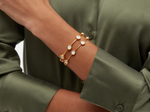 A close-up of a wrist wearing a gold bracelet with circular white stones, against a green shirt.
