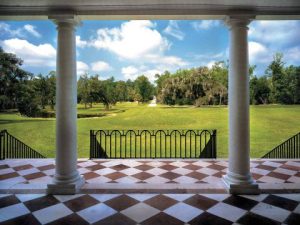 View from a portico with columns, overlooking a green landscape and pathway under a blue sky.