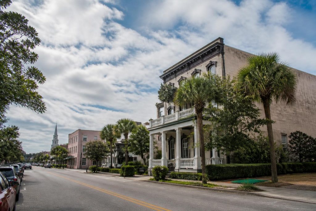Historic buildings line a tree-lined street under a partly cloudy sky in Summerville, SC.
