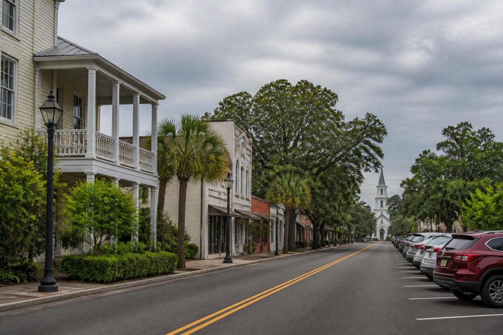Cloudy street view in Summerville, SC, featuring palm trees, historic buildings, and a church steeple in the distance.