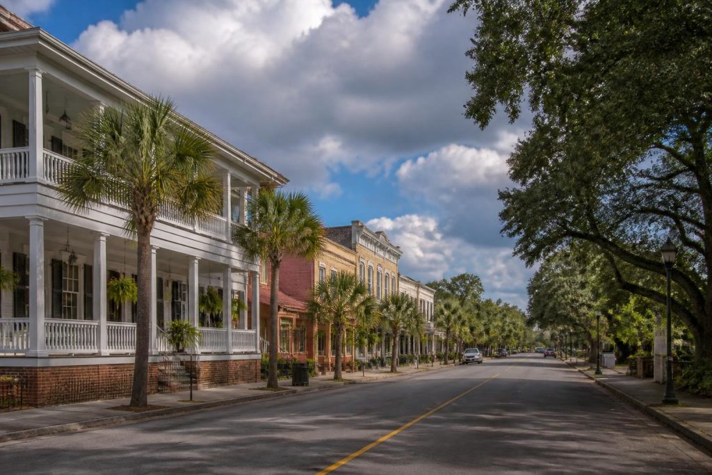 Historic buildings line a palm tree-lined street under a partly cloudy sky in Summerville, SC.