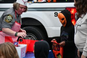 A woman in a uniform hands treats to a child wearing an orange mask, while others gather around.