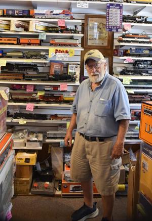 An older man stands in a model train shop, surrounded by shelves filled with various train models and boxes.